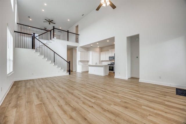 unfurnished living room with ceiling fan, light hardwood / wood-style floors, and a towering ceiling