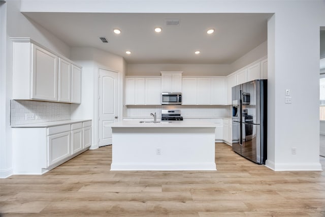 kitchen with white cabinetry, light hardwood / wood-style flooring, an island with sink, stainless steel appliances, and backsplash