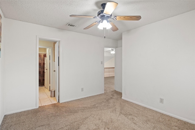 unfurnished bedroom featuring ceiling fan, light colored carpet, a textured ceiling, and ensuite bath