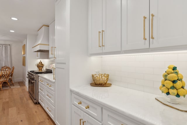 kitchen with white cabinetry, custom range hood, stainless steel stove, and backsplash