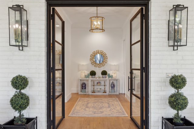 entrance foyer with brick wall, wood-type flooring, crown molding, and a notable chandelier