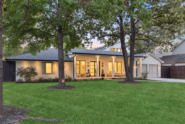 back house at dusk featuring a garage, a lawn, and a porch