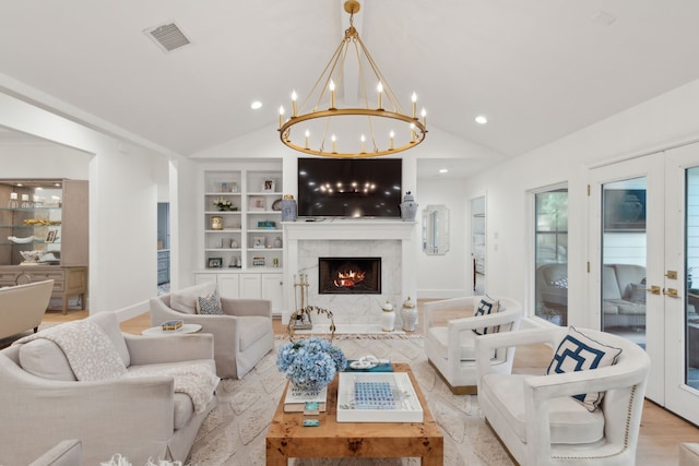 living room featuring a premium fireplace, light hardwood / wood-style floors, built in shelves, vaulted ceiling, and french doors