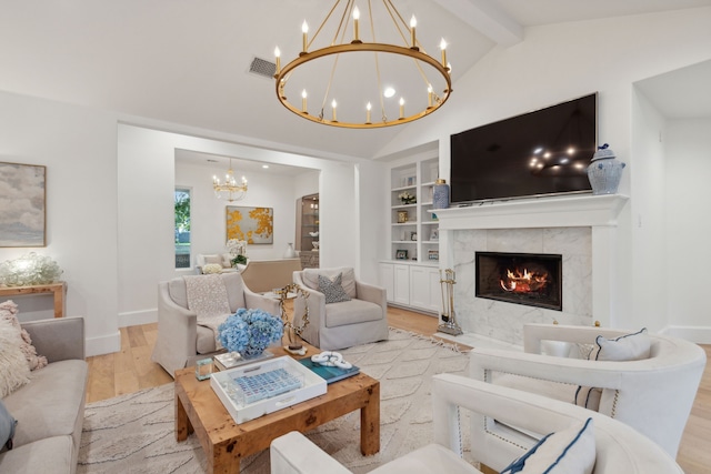 living room with lofted ceiling with beams, a tiled fireplace, a notable chandelier, light wood-type flooring, and built in shelves