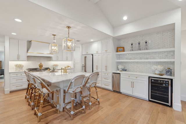 kitchen with white cabinets, custom exhaust hood, wine cooler, decorative backsplash, and a kitchen island with sink