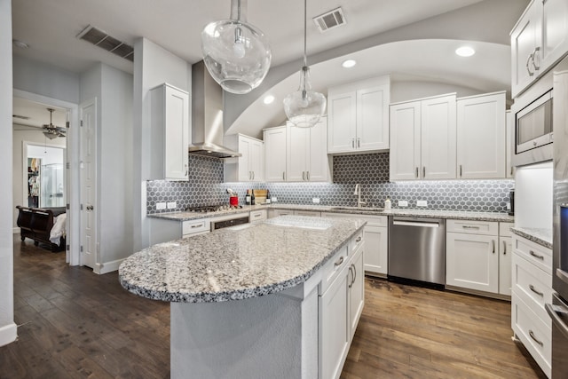 kitchen with a center island, wall chimney exhaust hood, white cabinetry, stainless steel appliances, and hanging light fixtures