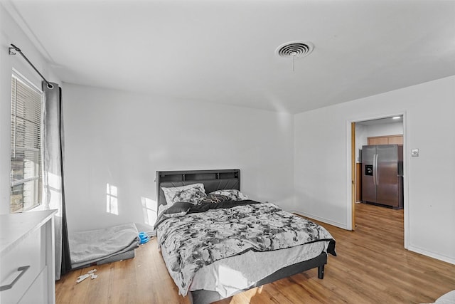 bedroom featuring stainless steel fridge with ice dispenser and light hardwood / wood-style floors