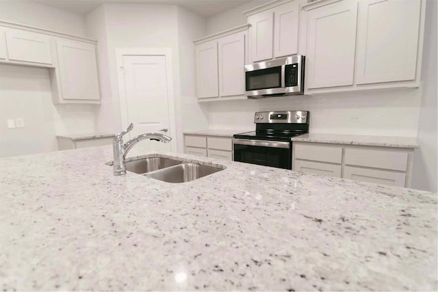 kitchen featuring sink, light stone countertops, white cabinets, and appliances with stainless steel finishes