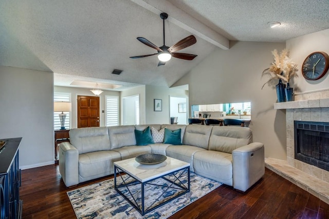 living room featuring a textured ceiling, dark wood-type flooring, a fireplace, lofted ceiling with beams, and ceiling fan