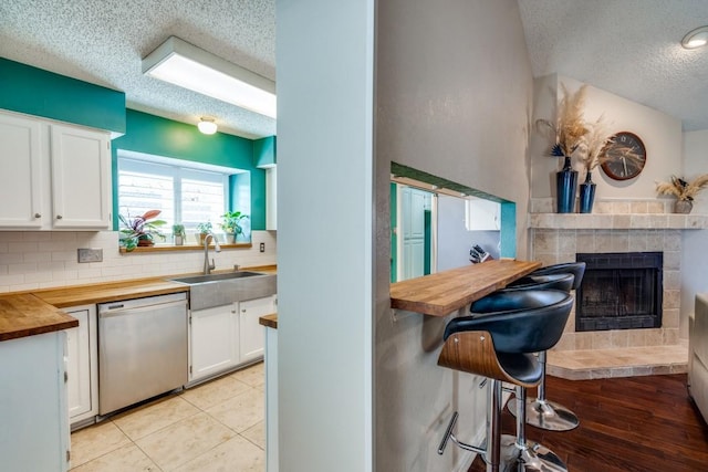 kitchen featuring a textured ceiling, stainless steel dishwasher, white cabinets, sink, and wood counters