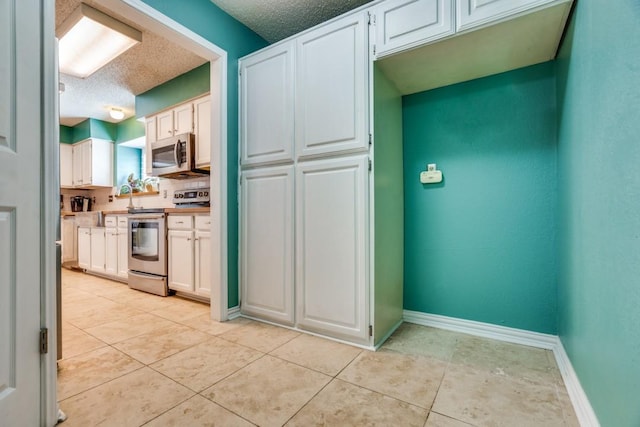 kitchen with white cabinets, a textured ceiling, light tile patterned floors, and stainless steel appliances