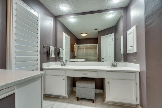 bathroom featuring a textured ceiling, tile patterned flooring, a shower with shower door, and vanity