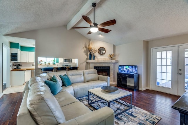 living room with a textured ceiling, a fireplace, dark hardwood / wood-style floors, lofted ceiling with beams, and ceiling fan