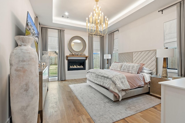 bedroom featuring light wood-type flooring, a notable chandelier, and a tray ceiling