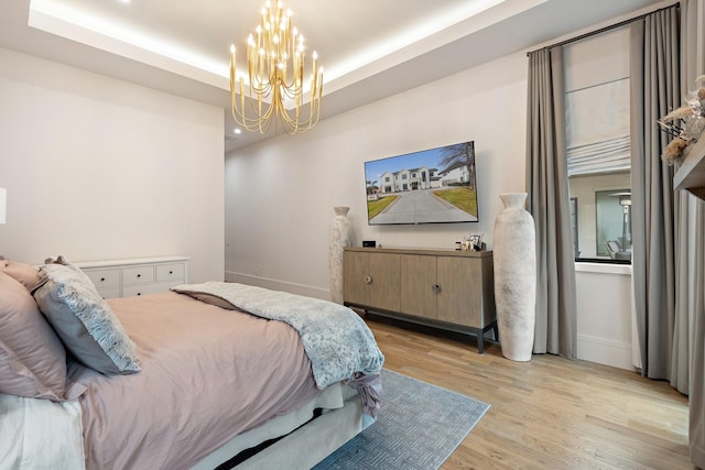 bedroom with a chandelier, light hardwood / wood-style flooring, and a tray ceiling