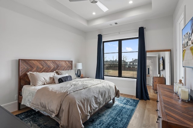 bedroom featuring ceiling fan, light hardwood / wood-style flooring, and a raised ceiling