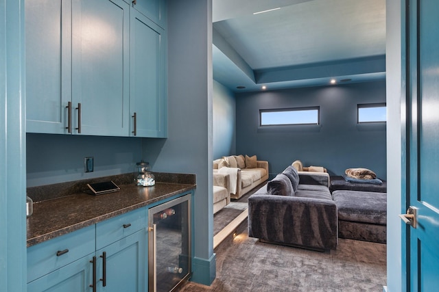 interior space with blue cabinetry, beverage cooler, a raised ceiling, and dark stone counters