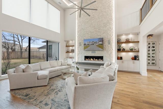 living room featuring built in features, light wood-type flooring, a high ceiling, and a stone fireplace