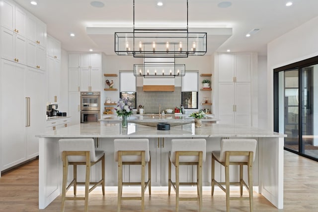 kitchen featuring light stone countertops, white cabinetry, a large island, and double oven