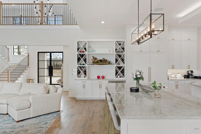 interior space featuring light wood-type flooring, white cabinetry, light stone counters, and pendant lighting