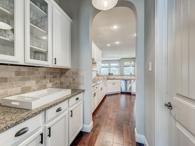 kitchen featuring dark wood-type flooring, white cabinetry, light stone counters, stainless steel dishwasher, and backsplash