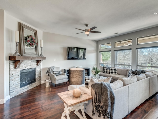 living room featuring dark hardwood / wood-style floors, ceiling fan, a stone fireplace, and a textured ceiling