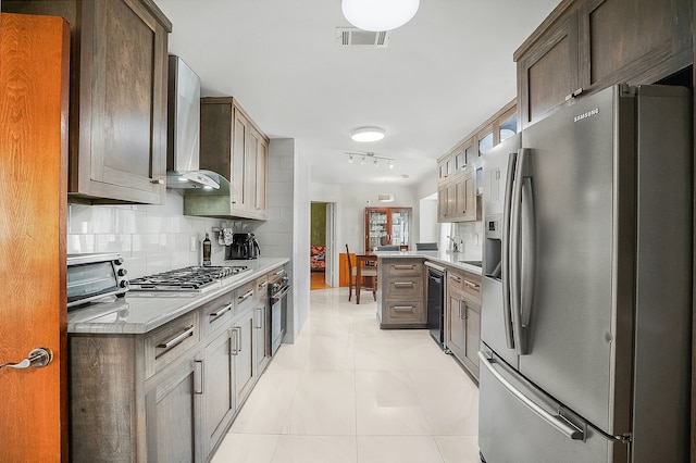 kitchen featuring wall chimney range hood, light tile patterned floors, rail lighting, stainless steel appliances, and decorative backsplash