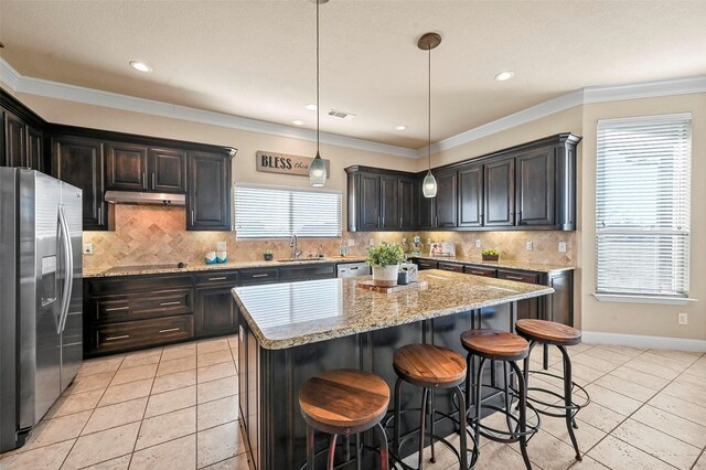 kitchen featuring a kitchen island, appliances with stainless steel finishes, light stone counters, and decorative light fixtures