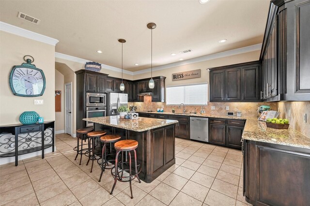 kitchen with crown molding, light stone counters, a center island, dark brown cabinets, and pendant lighting