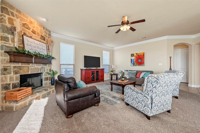 living room with crown molding, ceiling fan, and a stone fireplace