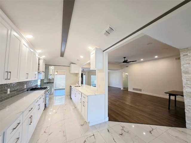 kitchen with white cabinetry, sink, stainless steel gas range oven, backsplash, and light stone counters