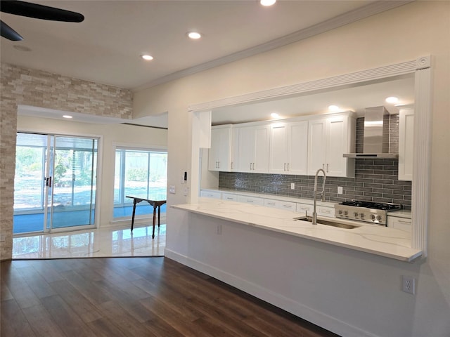 kitchen featuring wall chimney exhaust hood, sink, white cabinets, light stone counters, and stove