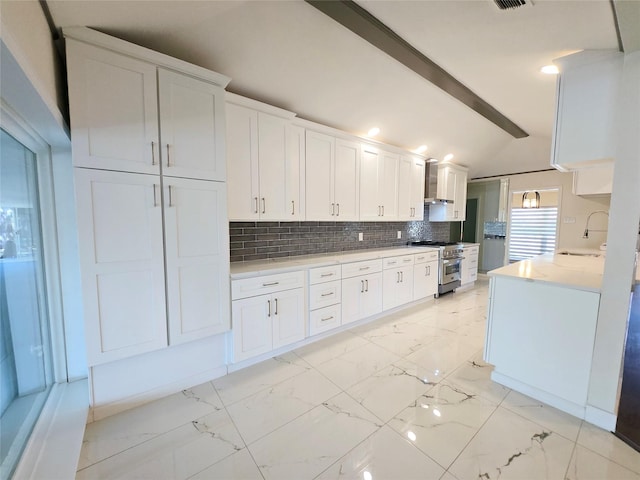 kitchen featuring tasteful backsplash, white cabinets, sink, vaulted ceiling with beams, and high end stove