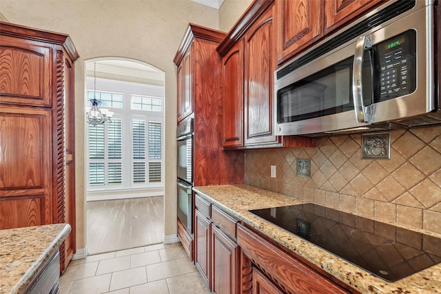 kitchen with black electric stovetop, an inviting chandelier, backsplash, light stone counters, and light tile patterned flooring