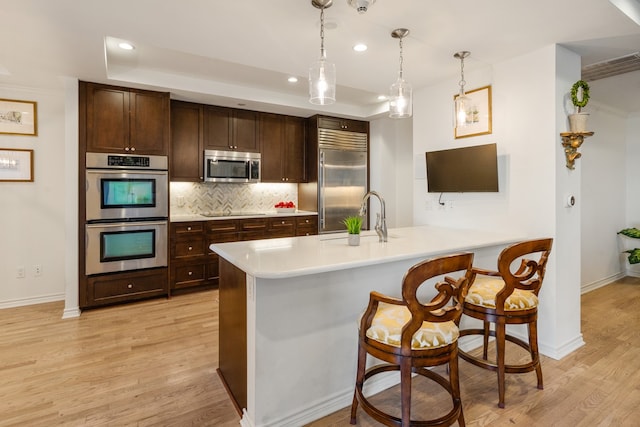 5909 Luther Ln Unit 2000, Dallas, TX 75225 - kitchen featuring tasteful backsplash, light wood-type flooring, dark brown cabinets, a peninsula, and stainless steel appliances