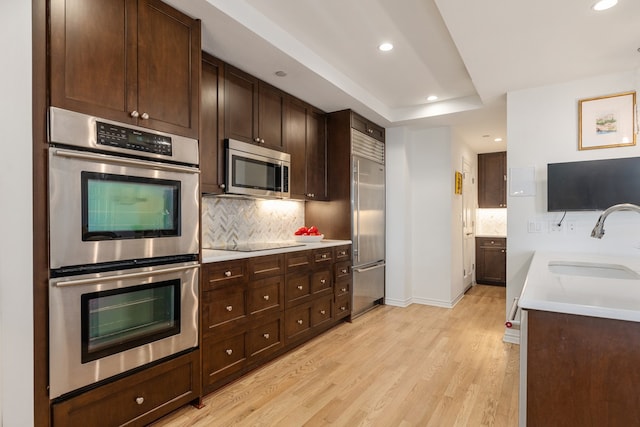 kitchen featuring sink, dark brown cabinets, light wood-type flooring, stainless steel appliances, and backsplash