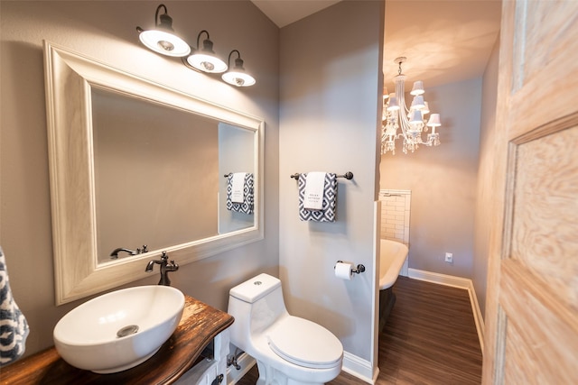 bathroom featuring a tub to relax in, a notable chandelier, toilet, wood-type flooring, and vanity