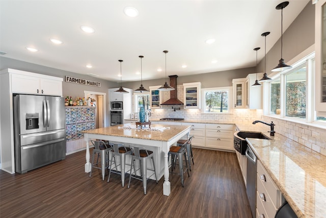 kitchen with appliances with stainless steel finishes, hanging light fixtures, white cabinets, a kitchen island, and a kitchen bar