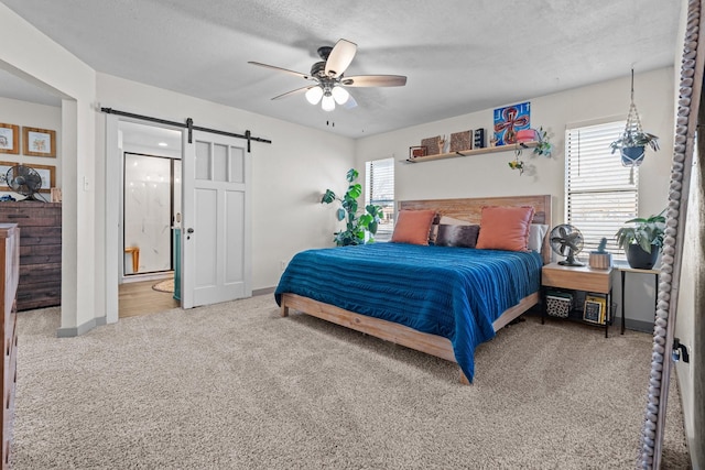 carpeted bedroom featuring ceiling fan, ensuite bath, a barn door, and a textured ceiling