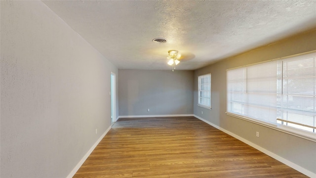 empty room with a healthy amount of sunlight, a textured ceiling, and light hardwood / wood-style floors