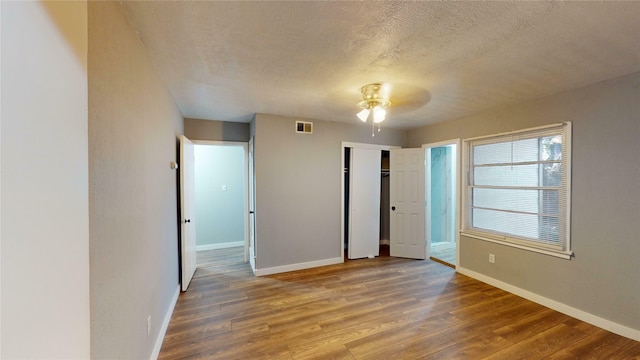 unfurnished bedroom featuring a closet, ceiling fan, hardwood / wood-style floors, and a textured ceiling