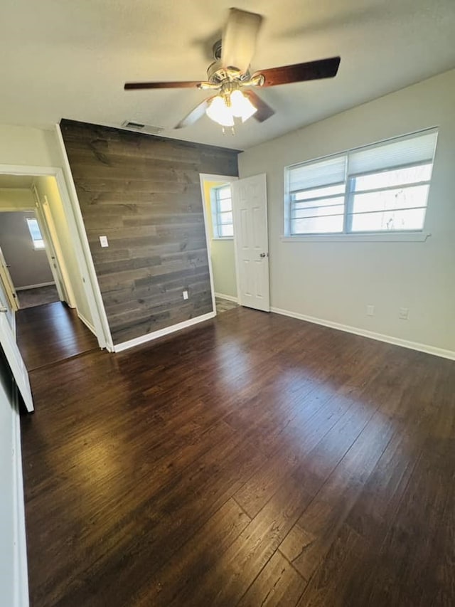 unfurnished room featuring dark hardwood / wood-style flooring, ceiling fan, a healthy amount of sunlight, and wood walls