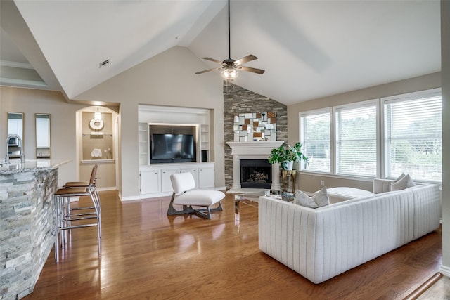 living room featuring high vaulted ceiling, a fireplace, hardwood / wood-style flooring, ceiling fan, and built in shelves