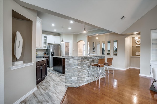 kitchen with a breakfast bar area, white cabinets, stainless steel refrigerator with ice dispenser, a center island with sink, and light hardwood / wood-style flooring