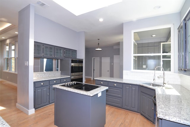 kitchen featuring light hardwood / wood-style floors, hanging light fixtures, black electric cooktop, sink, and a kitchen island