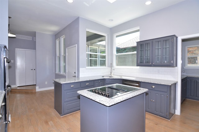 kitchen with light hardwood / wood-style floors, tasteful backsplash, black electric stovetop, a kitchen island, and light stone counters