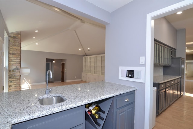 kitchen with light stone countertops, sink, light hardwood / wood-style flooring, and lofted ceiling