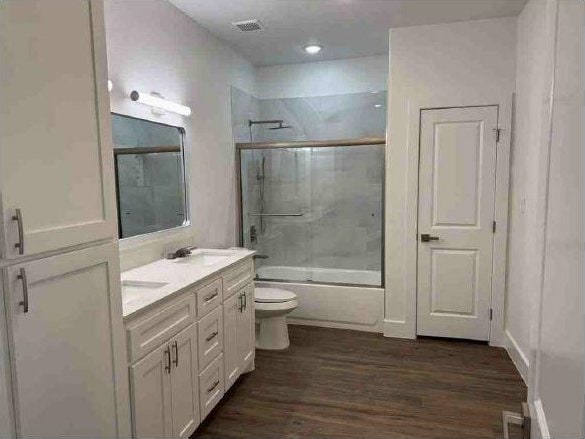 full bathroom featuring vanity, hardwood / wood-style flooring, enclosed tub / shower combo, and toilet