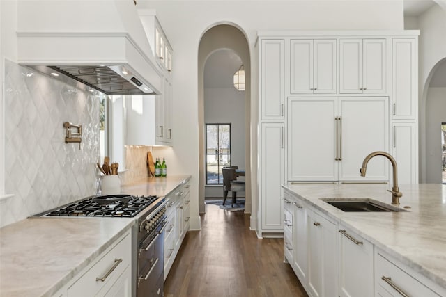 kitchen featuring custom range hood, sink, stainless steel stove, white cabinetry, and light stone countertops