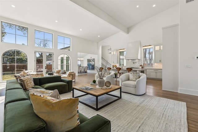 living room featuring a towering ceiling, light hardwood / wood-style flooring, beam ceiling, and a notable chandelier